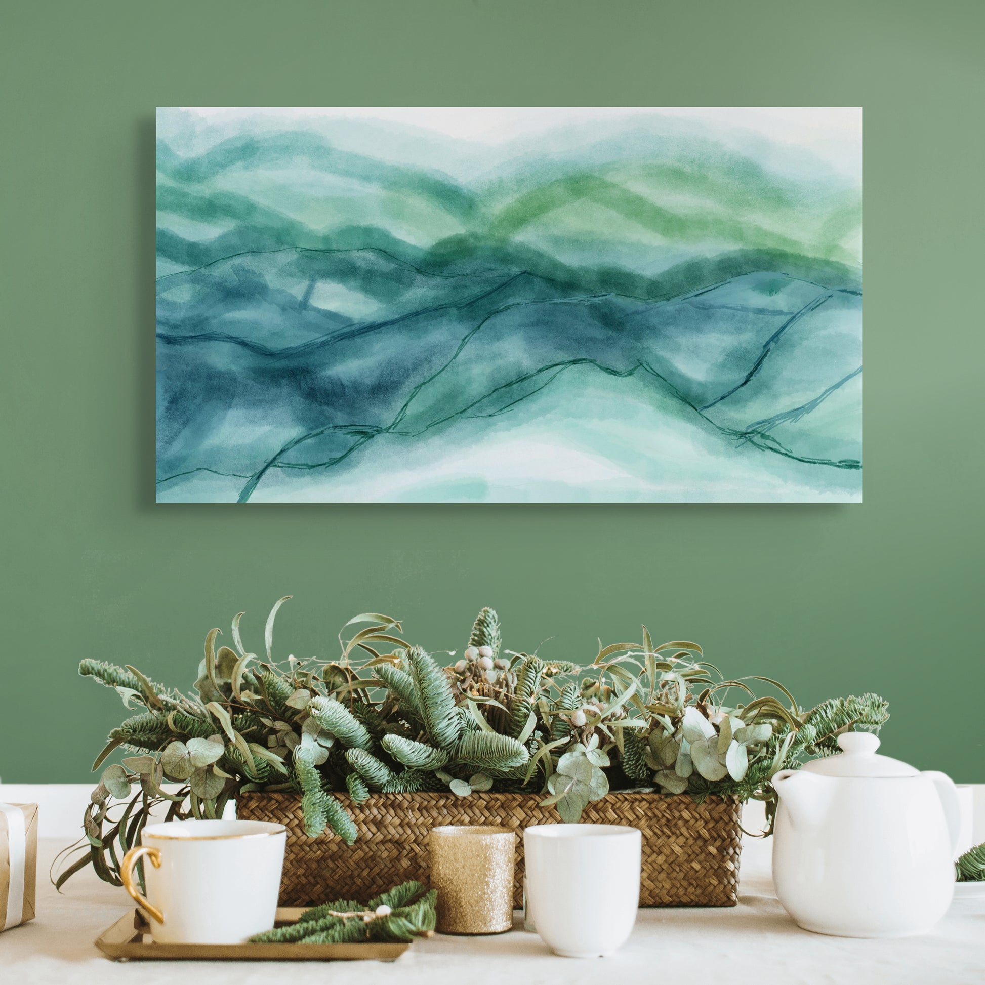 Decorative setup with a wicker basket of plants, white teapot, and cups against a green wall with abstract green and blue painting.