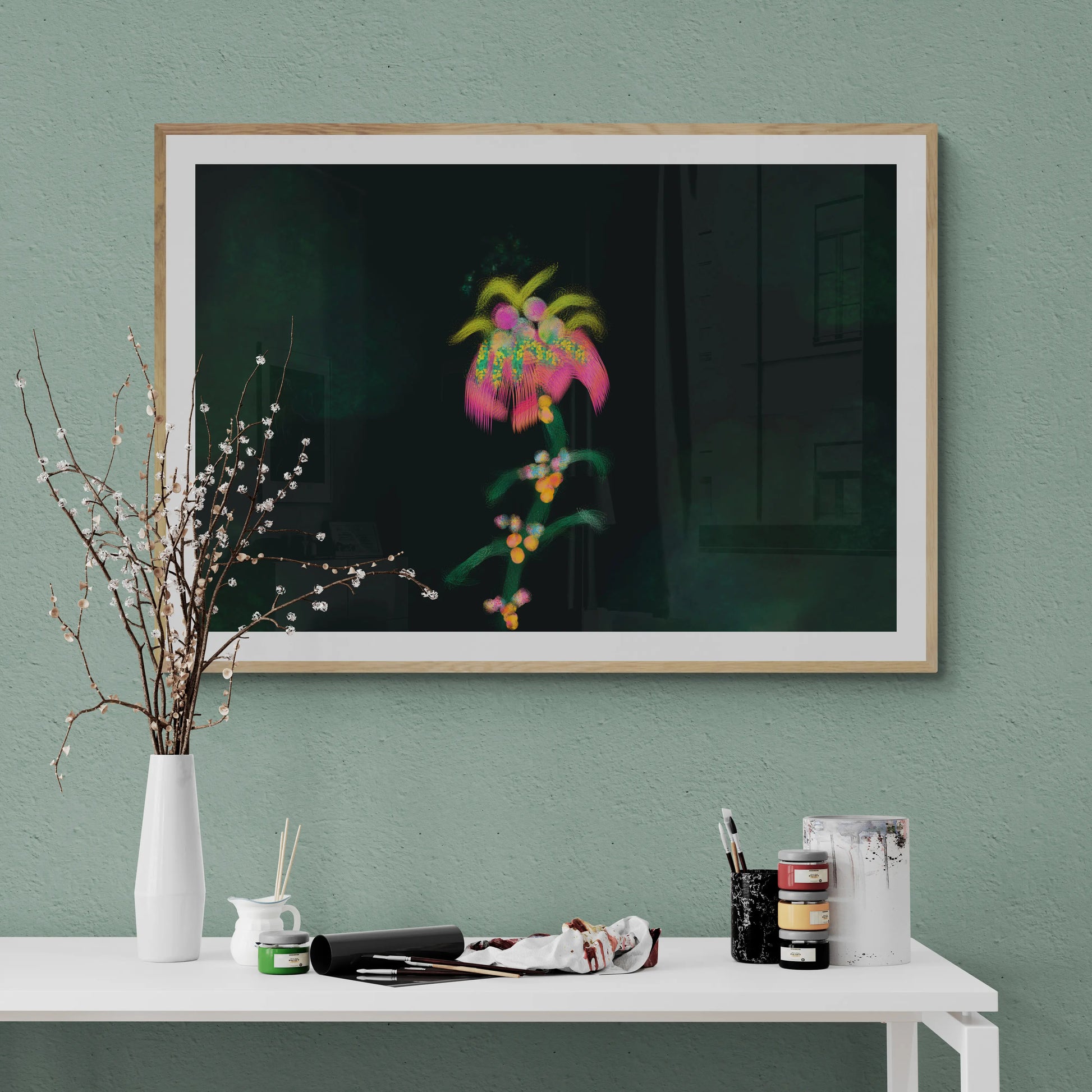 Framed artwork on a wall with a vase and art supplies on a table below.