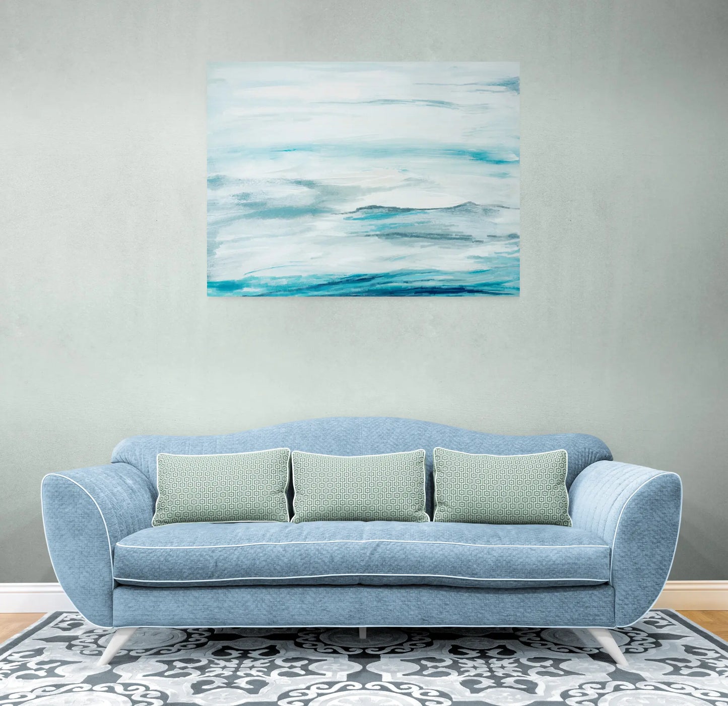 Blue sofa with green pillows in a room with abstract blue and white painting on the wall.