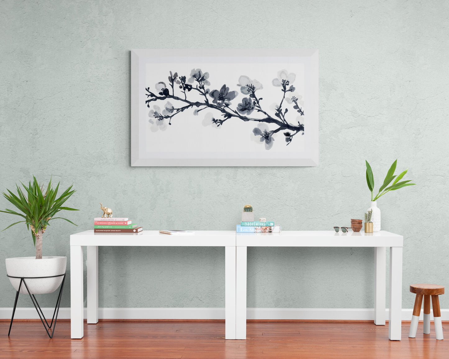 Modern interior with a white table, plants, and a floral painting on a light green wall.