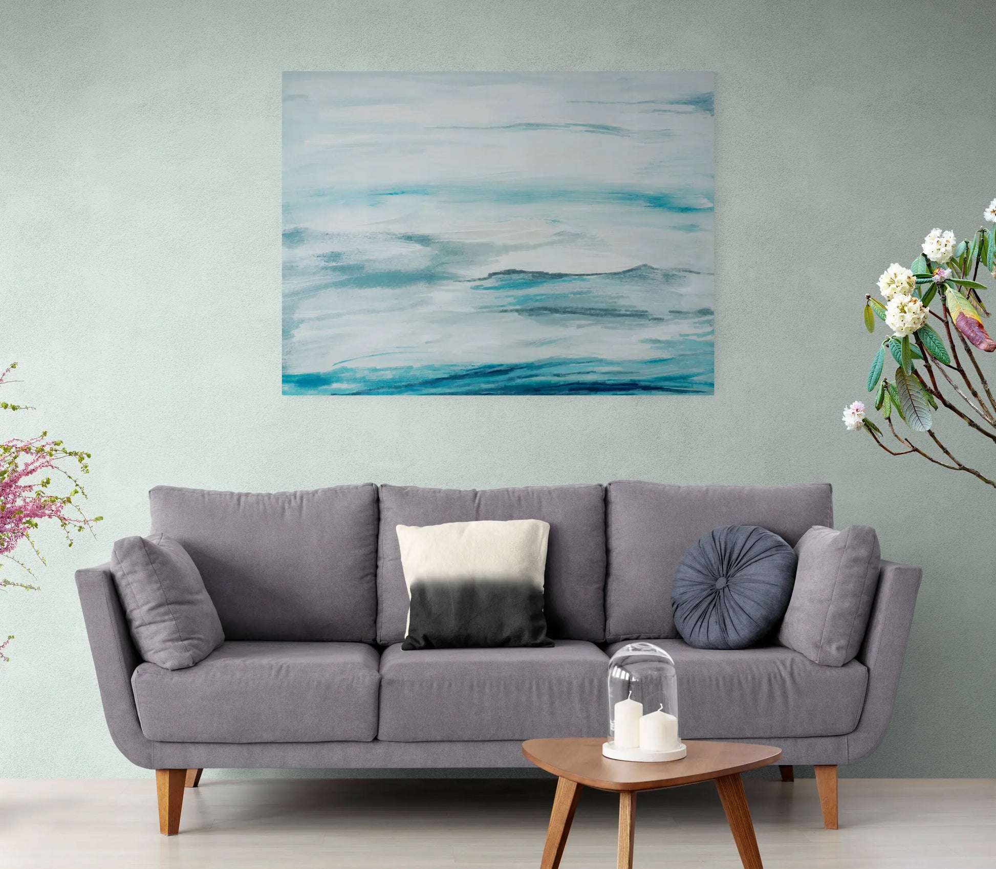 Gray sofa in a living room with a painting above it and a small table with candles in front.