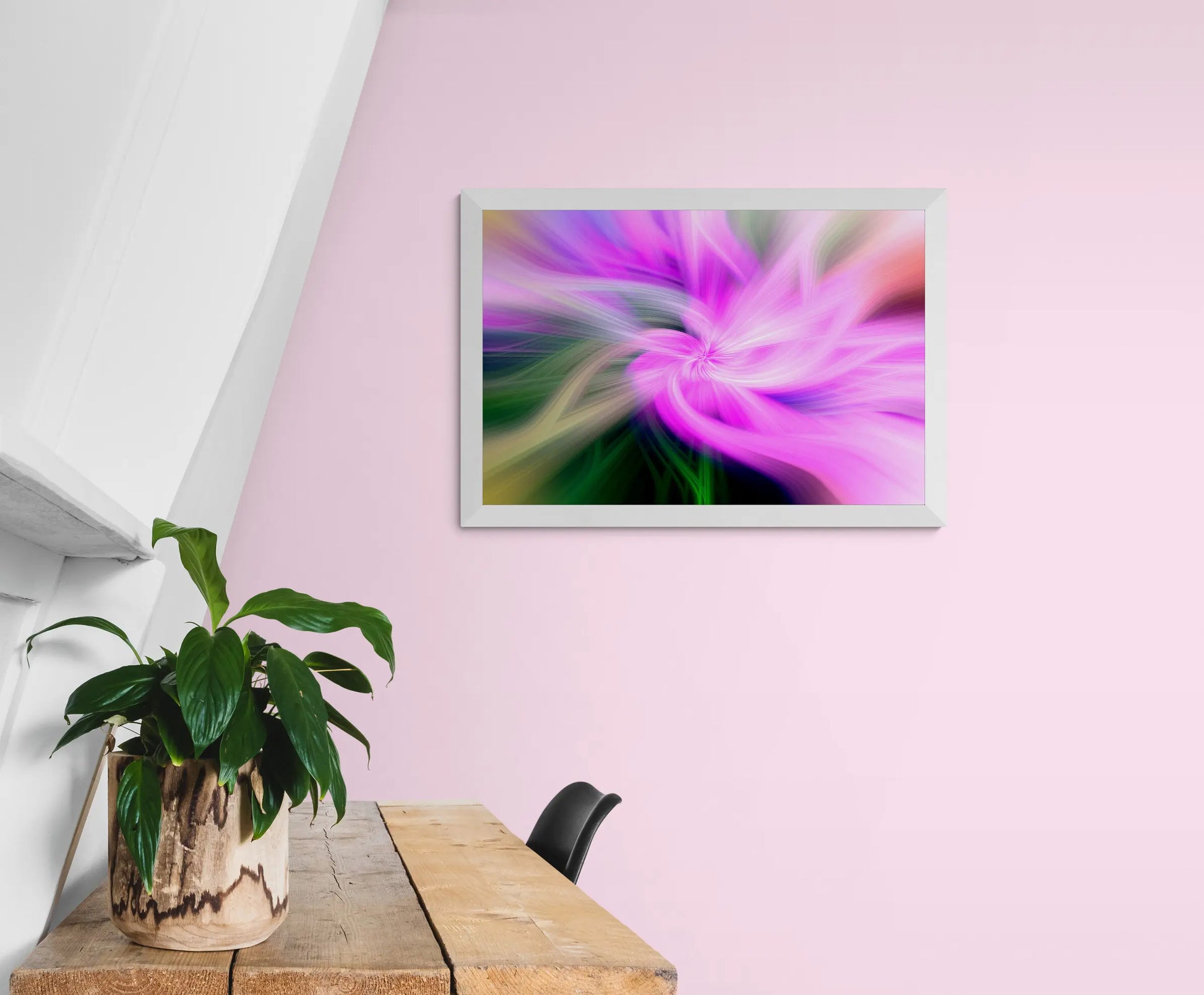 Framed abstract artwork of a pink flower on a pink wall above a wooden table with a plant.