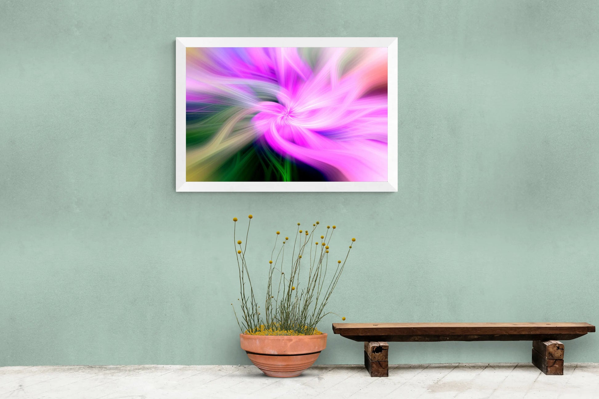 Framed abstract artwork with a pink flower on a green wall, next to a wooden bench and potted plant.